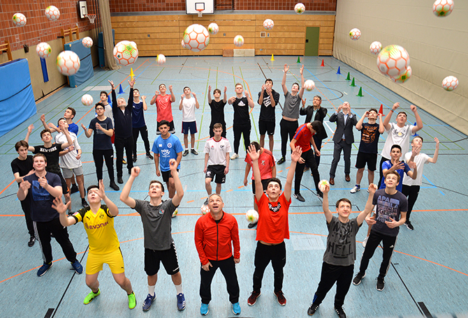 Schüler und Lehrer werfen die Fairen Fußbälle in die Höhe.
