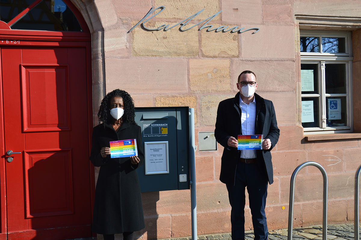Sandra Niyonteze und Peter Reiß stehen vor dem Rathaus mit einer Botschaft für Toleranz und gegen Rassismus