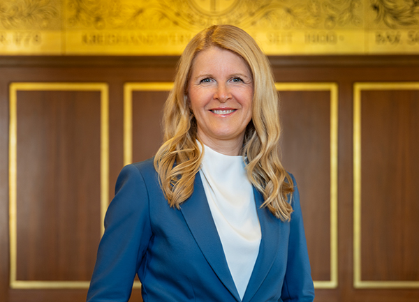 Frau Rother, blonde lange Haare, blaues Jacket und weiße Bluse, steht im Goldenen Saal